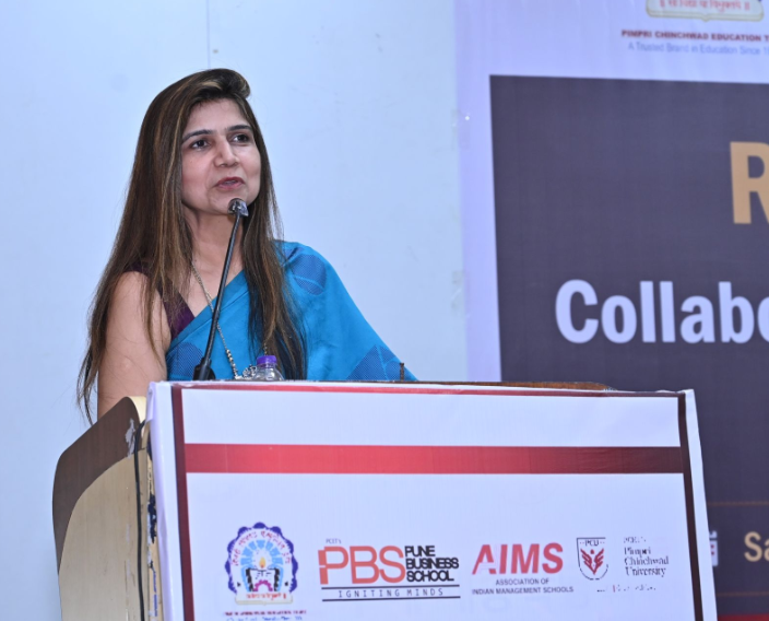 Dr. Minakshi Tyagi speaking at AIMS conference, PBS backdrop
